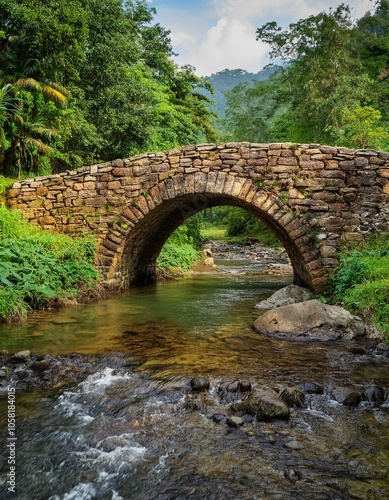 A stone arch bridge spans a tranquil stream in a lush forest setting.