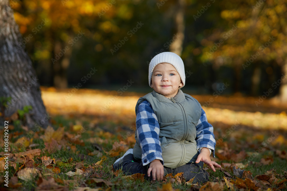 A toddler sits on autumn leaves, wearing a cozy beanie and warm vest, surrounded by fall foliage. The child's curious gaze captures the innocence and beauty of the autumn season outdoors. A toddler sits on autumn leaves, wearing a cozy beanie and warm vest, surrounded by fall foliage. The child's curious gaze captures the innocence and beauty of the autumn season outdoors.