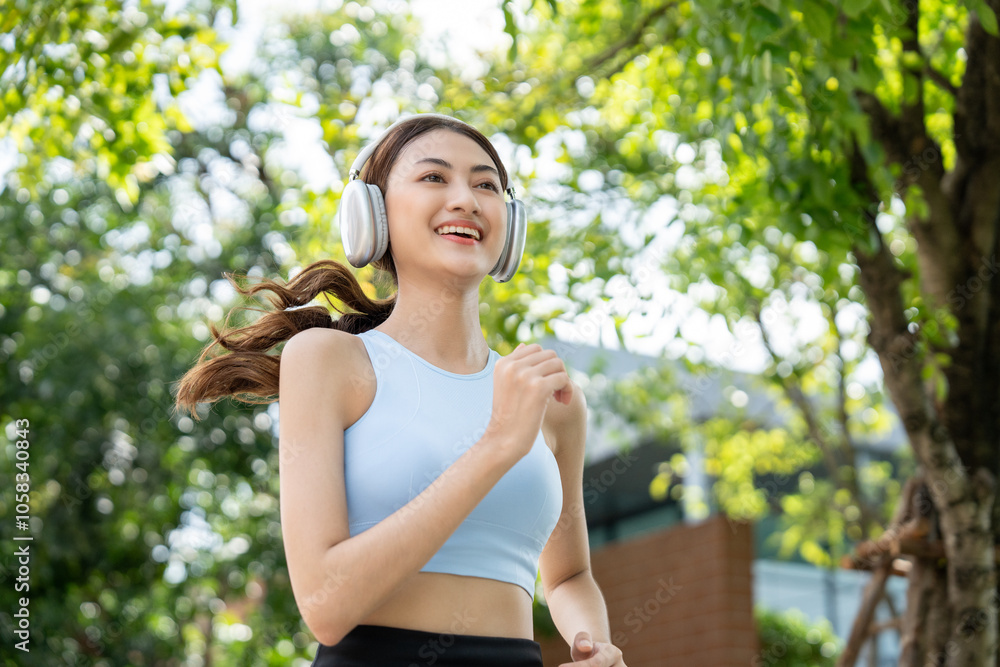 Happy slim beautiful woman wearing sportswear jogging in the park with sunrise. Young beautiful asian female in sportswear running outdoor. Workout exercise in the morning listen music with headphone