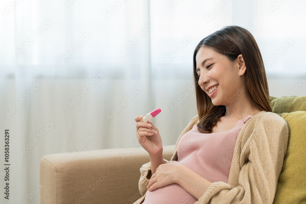 Happy pregnant young woman holding the pregnancy test kit and caressing her belly at home, happy motherhood waiting for childbirth, family planning and pregnancy with insurance for child health. Happy pregnant young woman holding the pregnancy test kit and caressing her belly at home, happy motherhood waiting for childbirth, family planning and pregnancy with insurance for child health.
