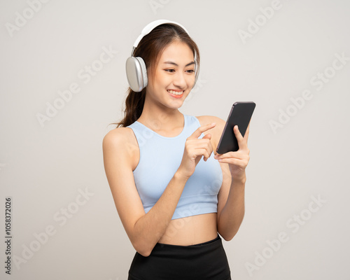 Young beautiful asian woman with sportswear choosing song with smartphone listen to music by headphone on isolated white background. Attractive Portrait sporty woman posing with cell phone