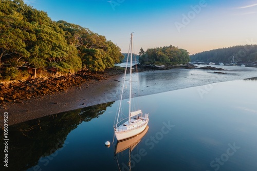 Boat moored in the calm Branch estuary during low tide at sunrise. The estuary is surrounded by forest, Phippsburg, Maine, United States. photo