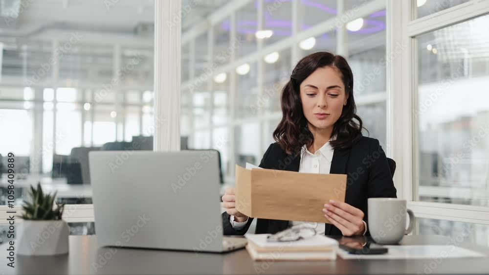Smiling happy businesswoman is sitting at her desk and reading a letter. Woman smiles as girl reads the good news. Great for themes of business, finance, success, and happiness. Smiling happy businesswoman is sitting at her desk and reading a letter. Woman smiles as girl reads the good news. Great for themes of business, finance, success, and happiness.