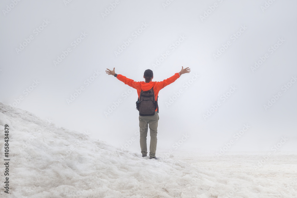Cold weather, snow on hills. Winter hiking. Climbing the mountains. Sport activity concept. Man hiker with backpack stands on top of mountain with his hands up. Cold weather, snow on hills. Winter hiking. Climbing the mountains. Sport activity concept. Man hiker with backpack stands on top of mountain with his hands up.