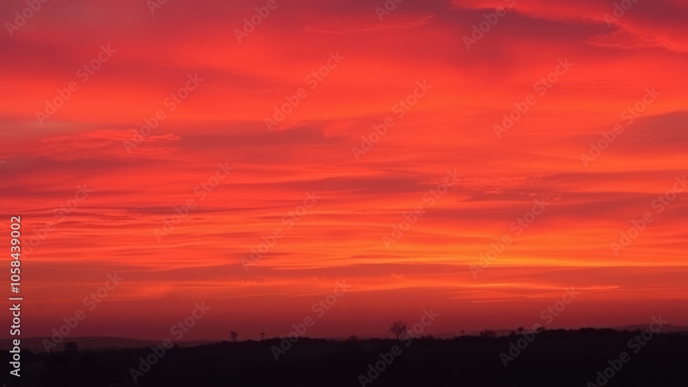 Vivid red sunset sky over a dark silhouette of rolling hills, creating a dramatic landscape