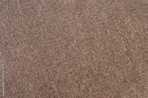 A gray-brown textured surface of a synthetic carpet with a close-up with rows of quilted knots with a diagonal slope to the right. Blank for the background in artworks.