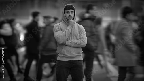 A reflective young man stands in a busy city street, immersed in the vibrant urban life