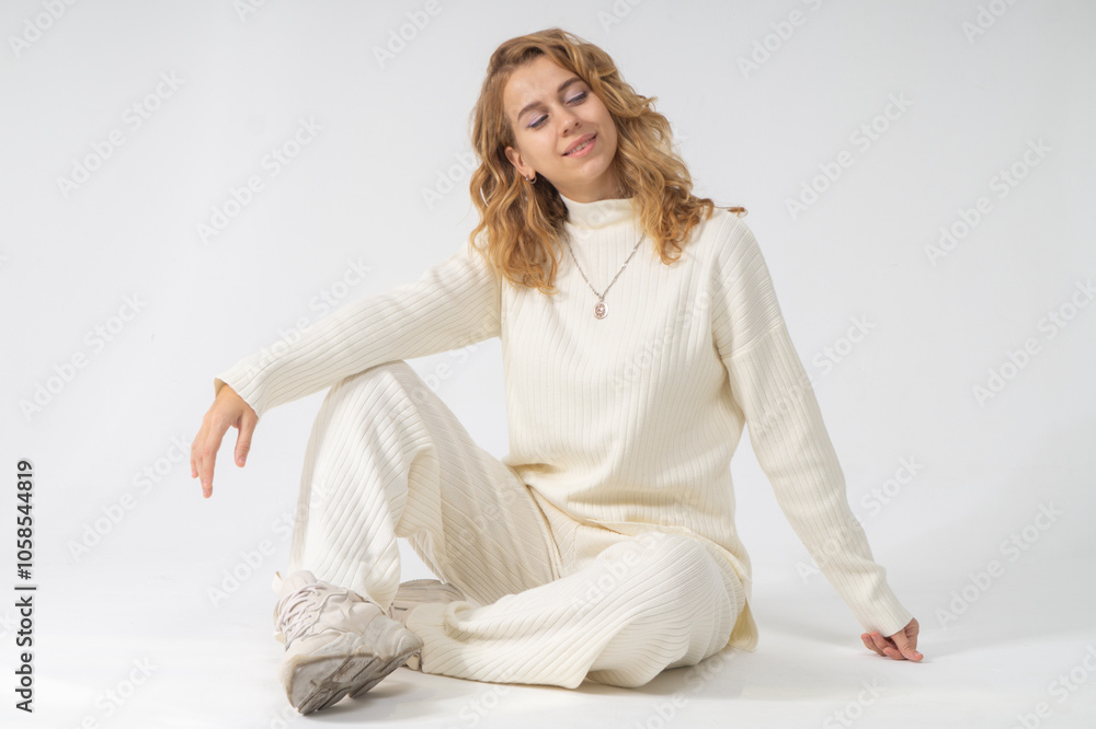 Cute young blonde girl sitting on a floor, white background, copy space Cute young blonde girl sitting on a floor, white background, copy space