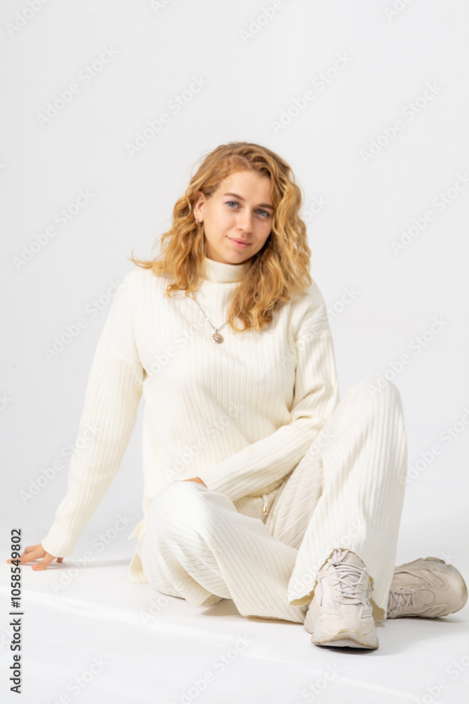 Cute young blonde girl sitting on a floor, white background, copy space Cute young blonde girl sitting on a floor, white background, copy space