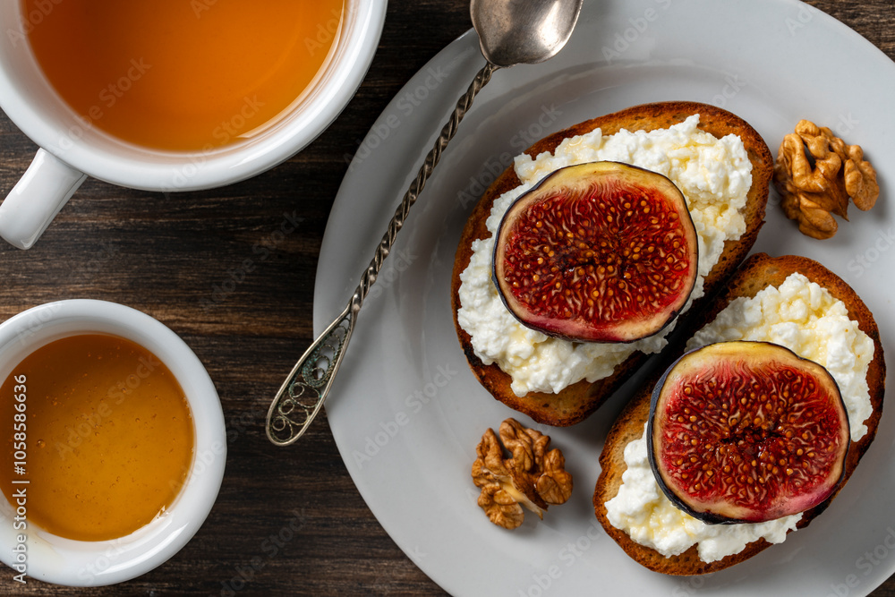 Φωτογραφία Two sandwiches with fresh fig slices, white cottage cheese, honey and walnuts on toast bread on a plate, top view, closeup