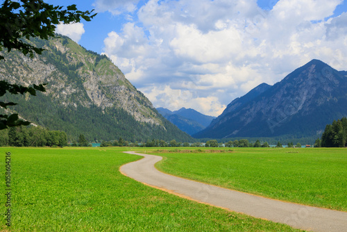 Field path between green mowed meadows towards Heiterwanger lake with mountains in the background on a sunny day with blue sky in Heiterwang, Austria photo