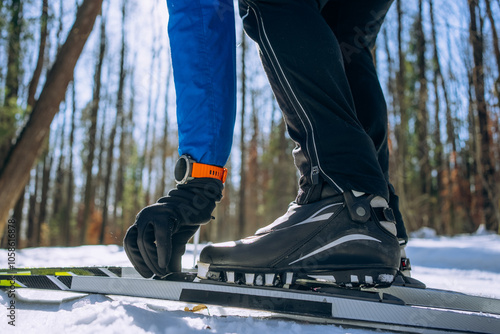 Foto Cross-country skier fastens his ski boot in a snowy forest, preparing for outdoo