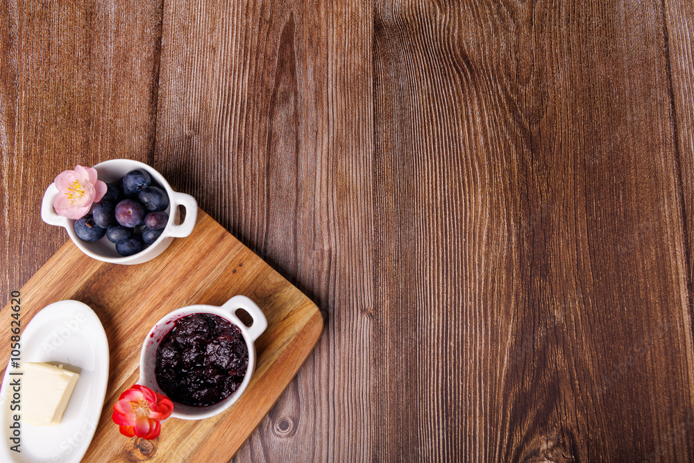 Dark wooden table with cutting board holding toast spread with blueberry jam and a butter dish, viewed from above in a rustic style Dark wooden table with cutting board holding toast spread with blueberry jam and a butter dish, viewed from above in a rustic style
