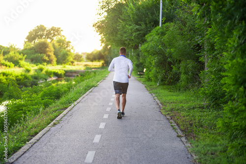 Young man running on a park road at sunset