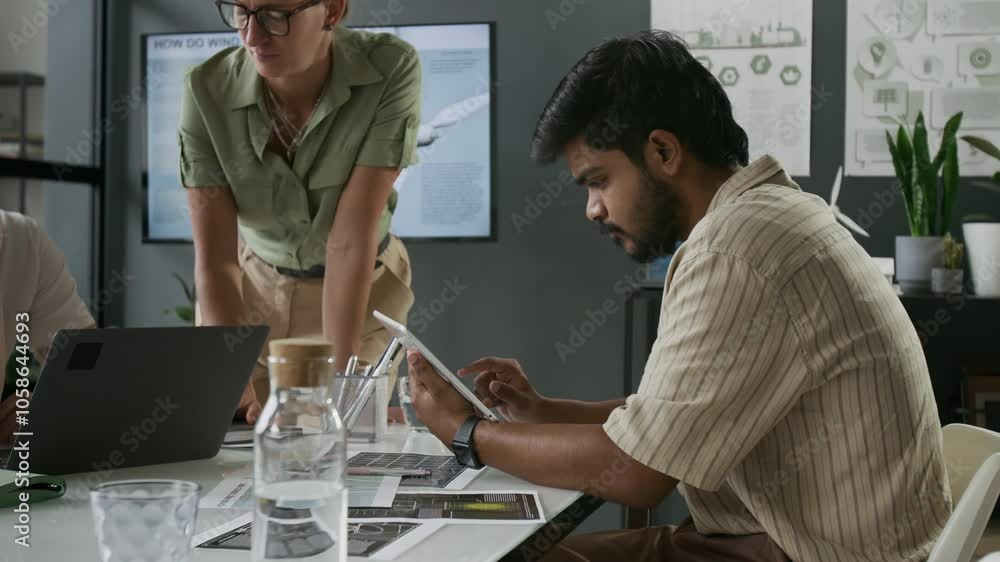 Indian man working on digital tablet during meeting with Caucasian colleagues in modern office Indian man working on digital tablet during meeting with Caucasian colleagues in modern office