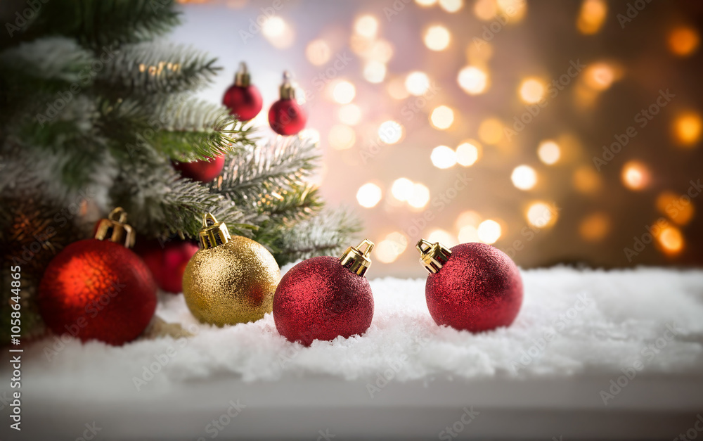 Red and gold Christmas ornaments rest in snow with a pine branch and bokeh lights in the background. Red and gold Christmas ornaments rest in snow with a pine branch and bokeh lights in the background.