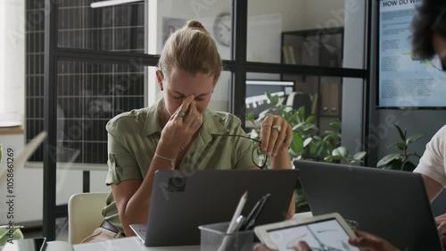Caucasian woman wearing eyeglasses getting tired after hours of work on laptop in modern office