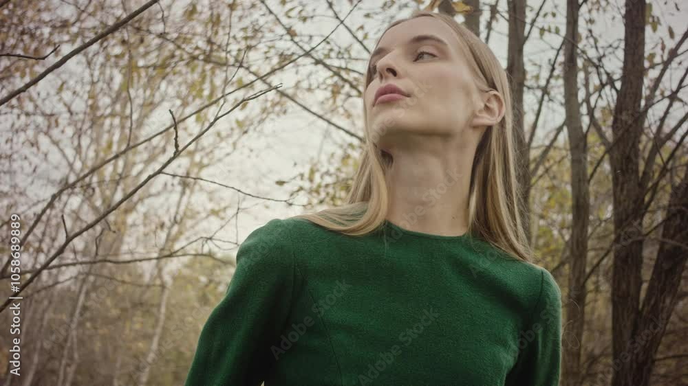 Woman with long blonde hair models a green dress in the forest. She closes her eyes and tilts her head back, enjoying the fresh air Woman with long blonde hair models a green dress in the forest. She closes her eyes and tilts her head back, enjoying the fresh air