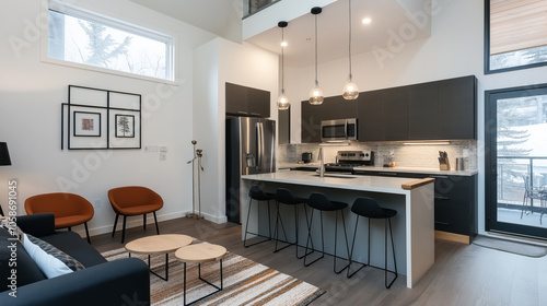 Modern open-plan kitchen and living room with high ceilings, featuring a sleek kitchen island with stools, stainless steel appliances, warm accent chairs, and contemporary lighting.