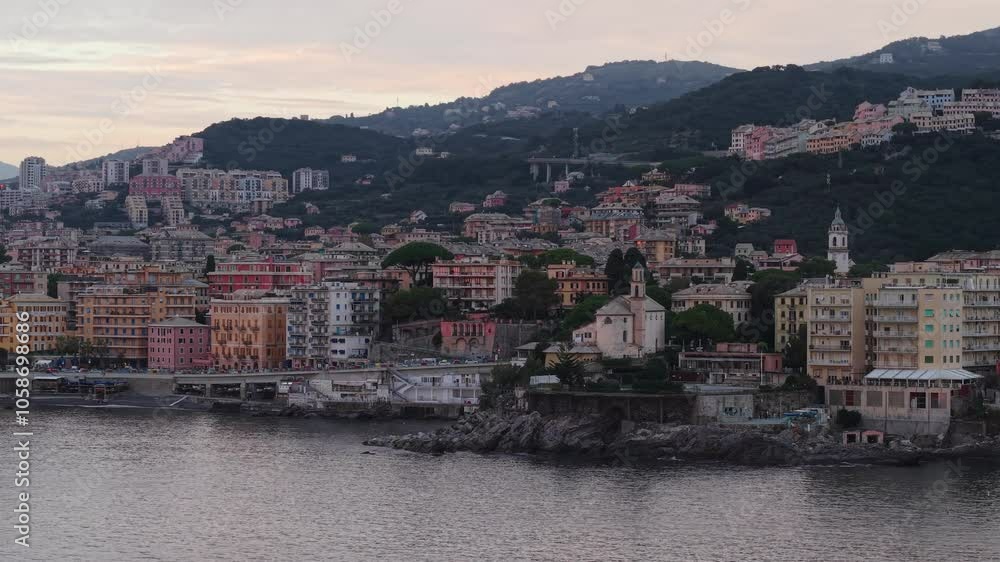 Genoa coastal town with colorful buildings and mountains at sunset over calm waters Genoa coastal town with colorful buildings and mountains at sunset over calm waters