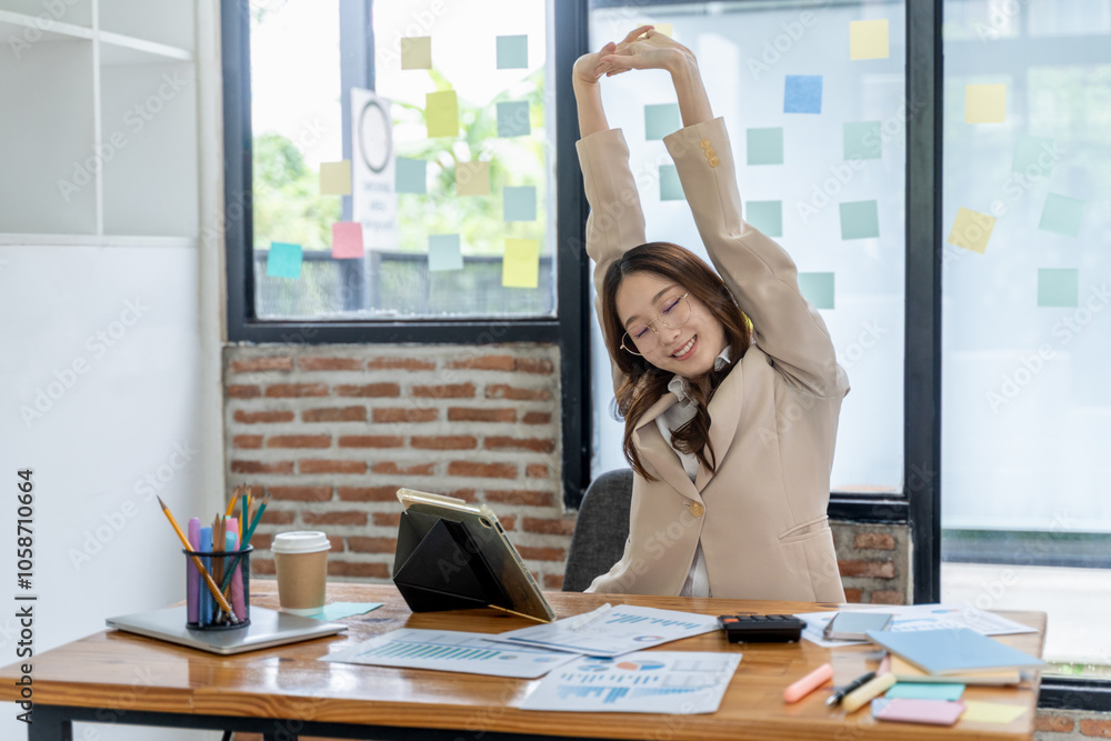 Tired young businesswoman stretching her arms and upper body while sitting at her office desk Tired young businesswoman stretching her arms and upper body while sitting at her office desk