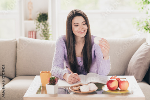 Photo of attractive young teen woman do homework eat snacks dressed purple outfit bright cozy day light home interior living room