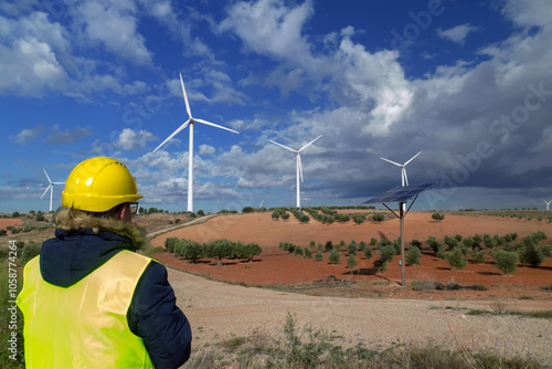 Engineer inspecting wind turbines and solar panel in rural landscape