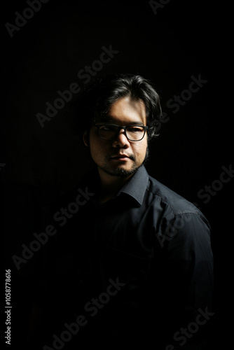 low key portrait of young Asian man in serious profile on black background