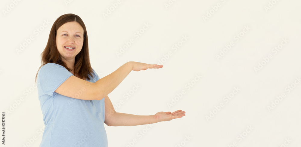 Young confident woman showing logo on empty space between arms. Smiling girl inviting or advertising promo deal, pointing hands right and looking at camera, white background. Young confident woman showing logo on empty space between arms. Smiling girl inviting or advertising promo deal, pointing hands right and looking at camera, white background.