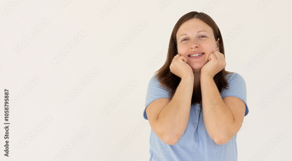 Headshot of pleased high spirit pretty female model, has warm pleasant smile, keeps hands under chin, wears blue t-shirt, isolated over white background. Happiness concept Headshot of pleased high spirit pretty female model, has warm pleasant smile, keeps hands under chin, wears blue t-shirt, isolated over white background. Happiness concept