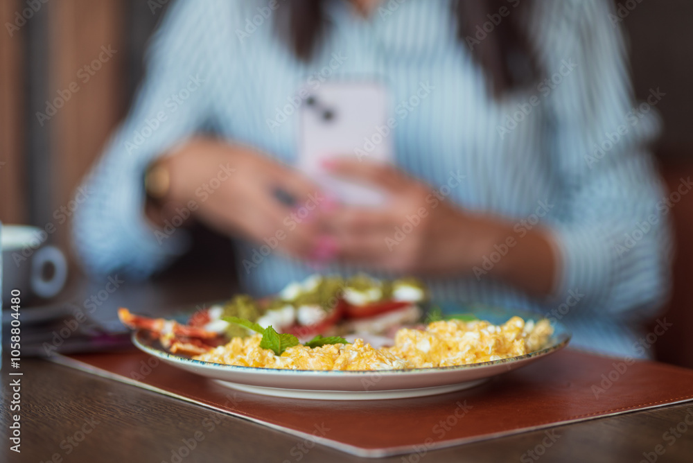 Woman taking a picture of scrambled eggs with smartphone in a restaurant Woman taking a picture of scrambled eggs with smartphone in a restaurant