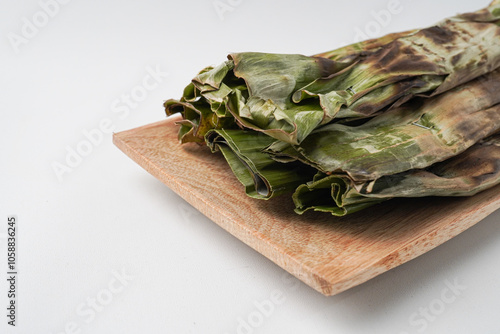 Otak-otak is a dish made from minced mackerel wrapped in banana leaves, grilled, and served with peanut sauce. Otak otak on wooden plate isolated over white backgrounds. Shot on 30 degree angle setup photo