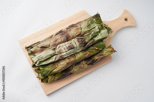 Otak-otak is a dish made from minced mackerel wrapped in banana leaves, grilled, and served with peanut sauce. Otak otak on wooden plate isolated over white backgrounds. Shot on flat lay setup photo