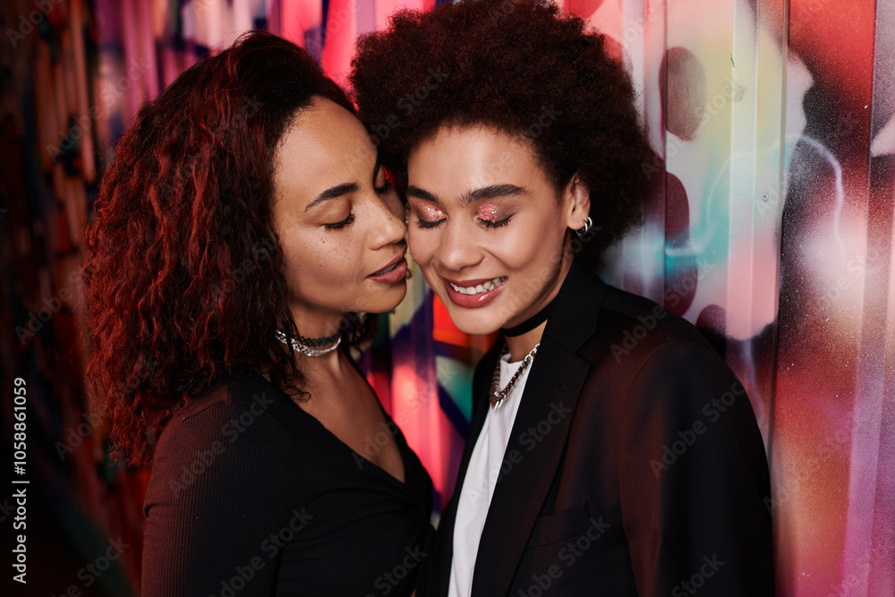 Two friends express warmth and happiness while posing closely amid colorful street art. Two friends express warmth and happiness while posing closely amid colorful street art.