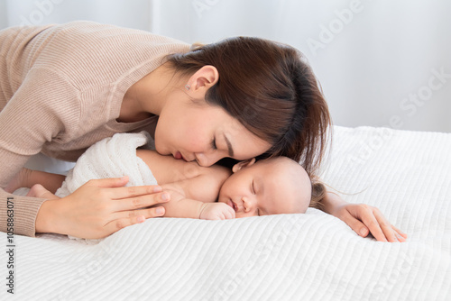 Selective focus of newborn baby deep sleeping on white bed. Asian beautiful mother hugging, cuddling and gently holding adorable infant hand with soft and care. Child healthcare sleep in mom's hand