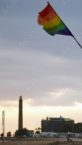 Winter Pride Maspalomas. Rainbow flags on Maspalomas Gay Beach waving in front of the lighthouse at sunset. Vertical photo