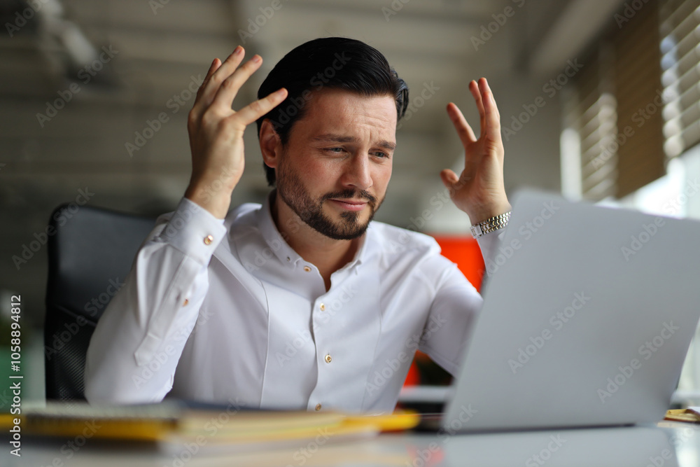 A man is sitting at a desk with a laptop in front of him. He is angry and frustrated, possibly due to a work-related issue A man is sitting at a desk with a laptop in front of him. He is angry and frustrated, possibly due to a work-related issue