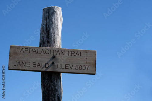 A trail sign along the Appalachian trail provides the elevation of Jane Bald in the western North Carolina mountains. A cloudless blue sky provides a backdrop to the sign. Horizontal.