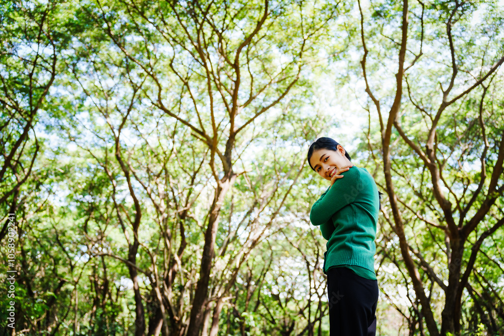 Young Asian woman sits under a shady tree in a park, enjoying her free time in nature. She breathes deeply, refreshing herself, surrounded by leaves and the tranquility of greenery. Young Asian woman sits under a shady tree in a park, enjoying her free time in nature. She breathes deeply, refreshing herself, surrounded by leaves and the tranquility of greenery.