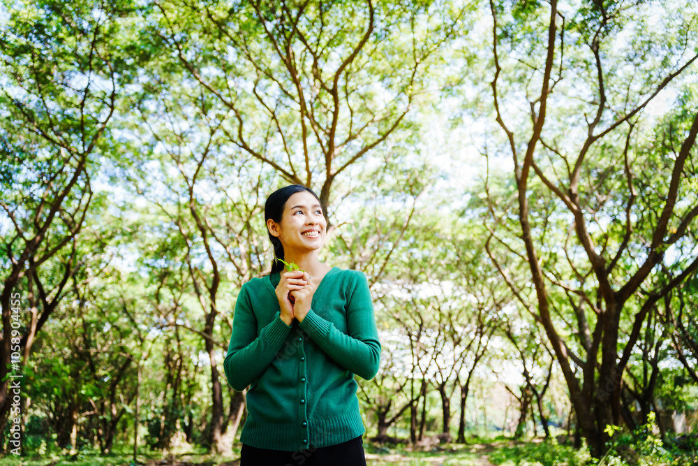 Young Asian woman sits under a shady tree in a park, enjoying her free time in nature. She breathes deeply, refreshing herself, surrounded by leaves and the tranquility of greenery. Young Asian woman sits under a shady tree in a park, enjoying her free time in nature. She breathes deeply, refreshing herself, surrounded by leaves and the tranquility of greenery.