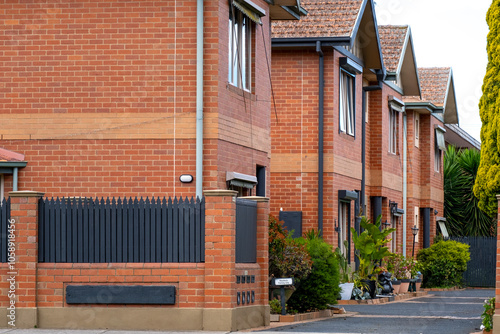 A row of older brick townhouses with repetitive architectural design and uniform terracotta roofing in a suburban residential neighborhood of Australia. Exterior of multi-family housing units.