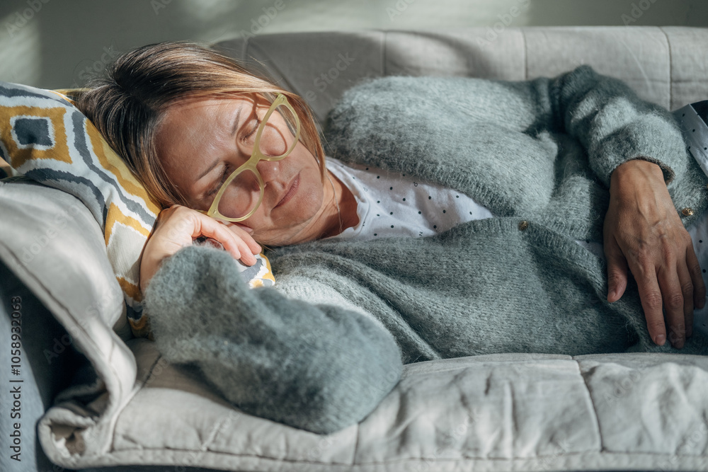 Mature woman is lying on couch at home closed eyes. Middle aged woman is tired and exhausted. Health problems, suffers migraine, high blood pressure, aging process or menopause concept. Mature woman is lying on couch at home closed eyes. Middle aged woman is tired and exhausted. Health problems, suffers migraine, high blood pressure, aging process or menopause concept.