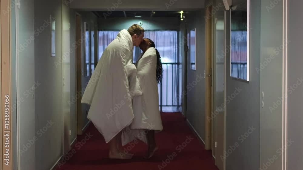 A happy loving couple stands in a dark hotel corridor, wrapped in white blankets. A beautiful wife and a handsome husband are enjoying a tender moment spent together. Young lovers on a date in a hotel A happy loving couple stands in a dark hotel corridor, wrapped in white blankets. A beautiful wife and a handsome husband are enjoying a tender moment spent together. Young lovers on a date in a hotel