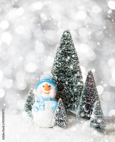 Toy Snowman on snow among fir trees with snowfall. Holiday greeting card template for Christmas or New Year