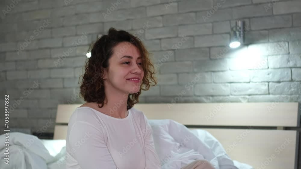 Happy sleepy young adult woman waking up, sitting in comfortable bed early in the morning. Positive beautiful girl stretches enjoying early good morning in cozy bedroom. Fresh lazy lady waking up at Happy sleepy young adult woman waking up, sitting in comfortable bed early in the morning. Positive beautiful girl stretches enjoying early good morning in cozy bedroom. Fresh lazy lady waking up at