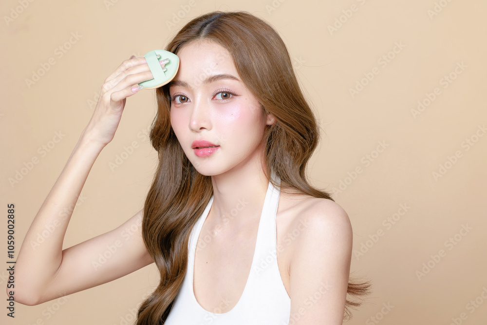 Young Asian beauty woman curly long hair with korean makeup style touch her face and perfect skin using puff on isolated beige background. Facial treatment, Cosmetology, plastic surgery. Young Asian beauty woman curly long hair with korean makeup style touch her face and perfect skin using puff on isolated beige background. Facial treatment, Cosmetology, plastic surgery.