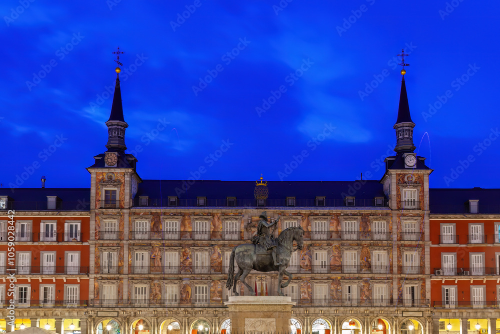 Illuminated at twilight, Madrid's historic Plaza Mayor showcases intricate architecture and the bronze statue of King Philip III, a captivating symbol of Spain's cultural heritage.