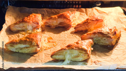 Golden brown cheese-filled pastries baking on parchment paper in an oven.