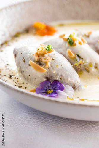 Kibbeh in creamy white sauce garnished with nuts and fresh herbs.