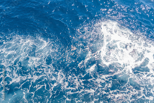 Sunlight glistens on deep blue ocean waves, with seafoam adding a dynamic texture and sparkle. photo